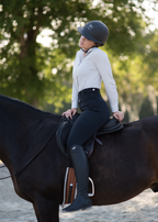 Woman sitting on a horse wearing black knee patch breeches and a white shirt. 